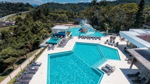 Una gran piscina con tobogán acuático, rodeada de sillas de descanso y una zona cubierta.