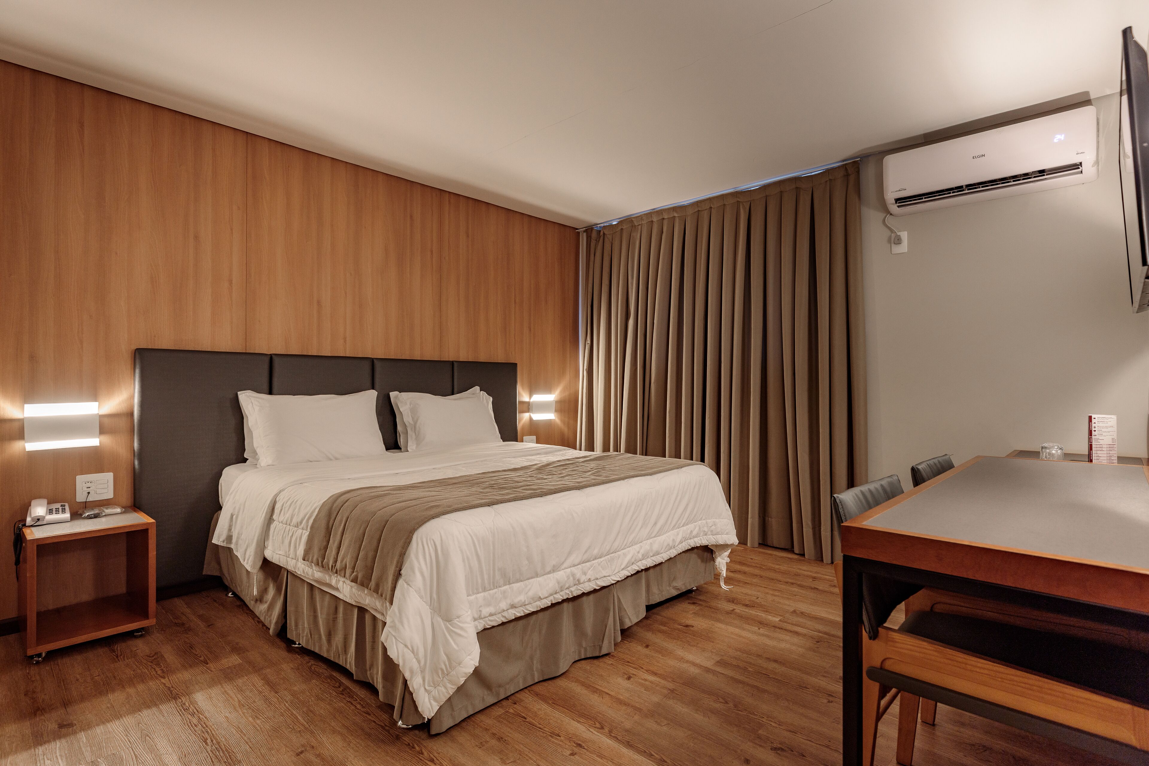 Una camera d'albergo con un letto, un comodino e una scrivania con sedie.
