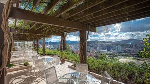 Una terraza con mobiliario exterior, vistas a un paisaje urbano y una pérgola cubierta de follaje.