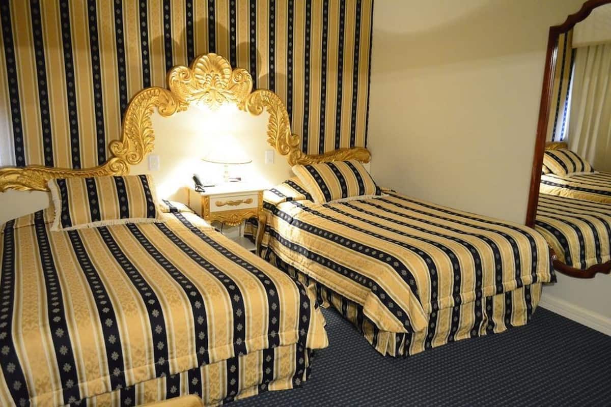A hotel room with two beds, a large mirror, and a nightstand with a lamp.