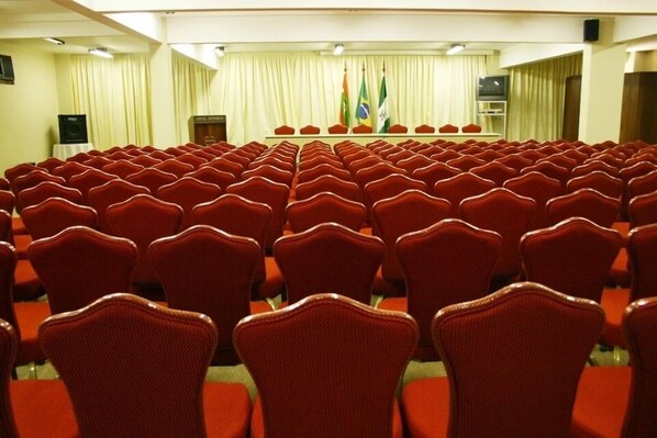 A conference room with rows of red chairs, a podium, and flags. - Hotel Bertaso (CHAPECO)