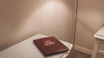 A corner of a hotel room with a white bedside table, a red book, and a floor lamp.