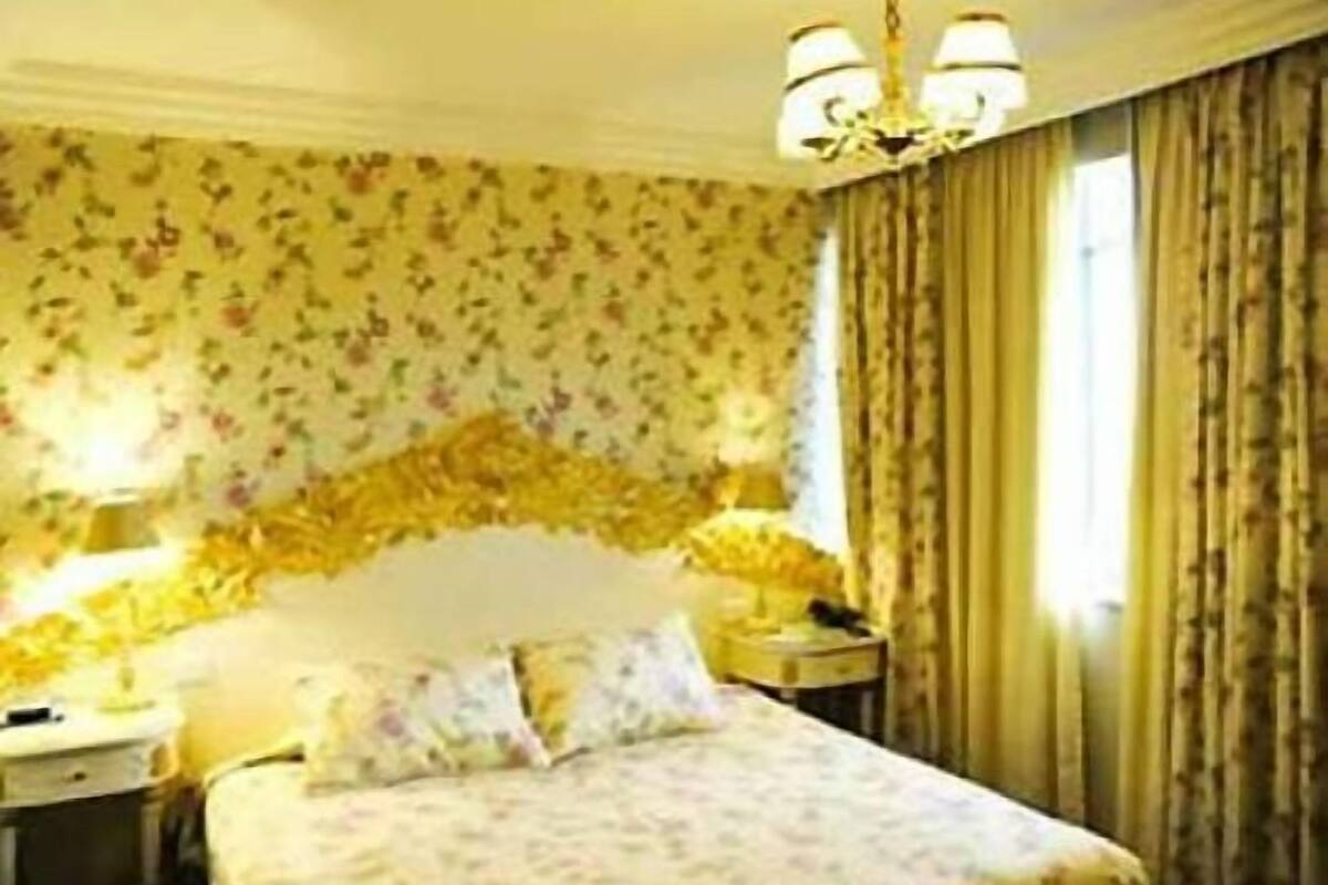 A hotel room with a bed, a nightstand, a lamp, and a chandelier.