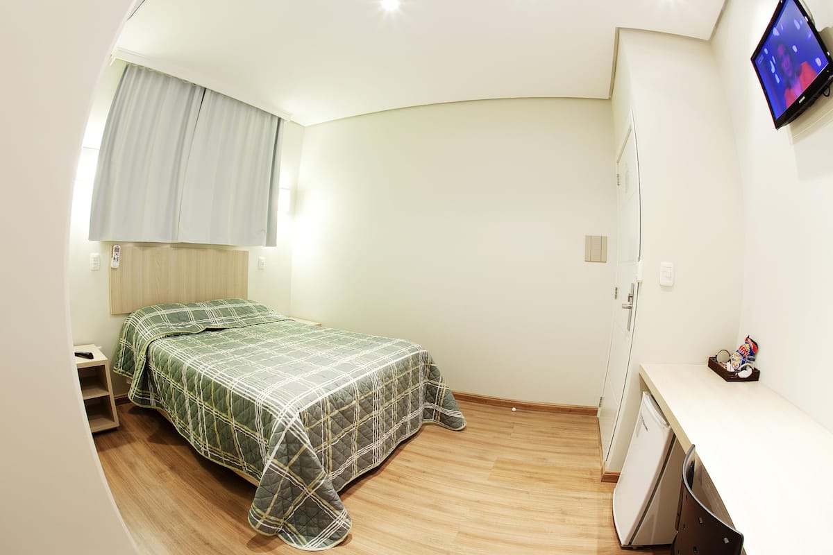 A bedroom with a bed, a desk, a television, and a wardrobe.