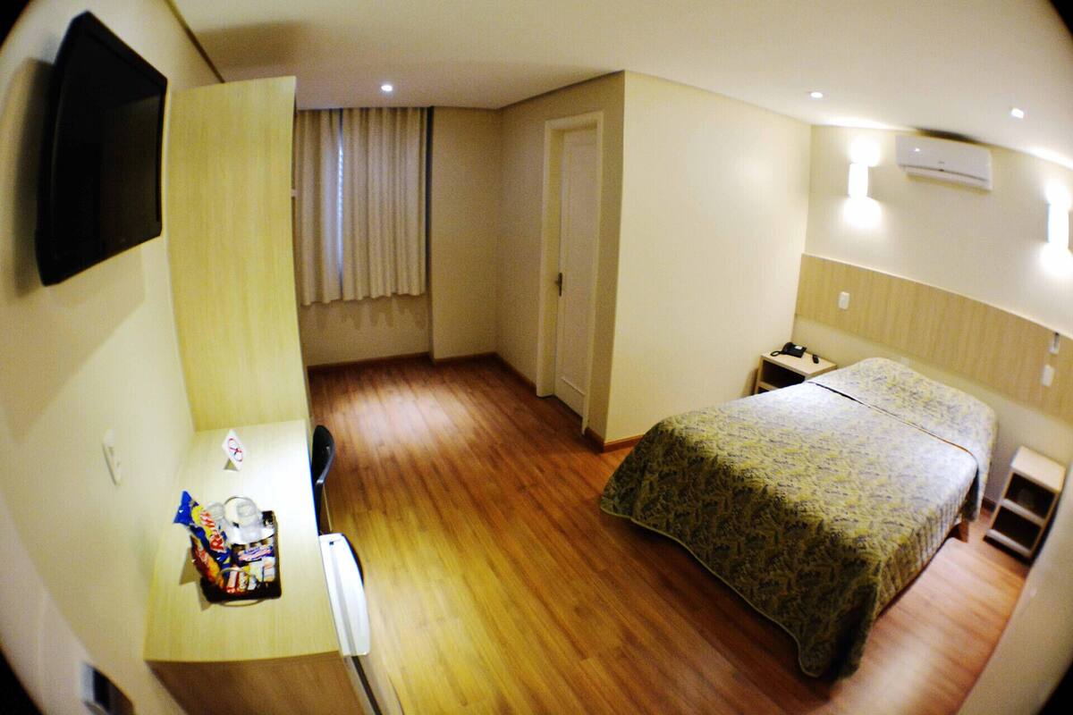 A compact hotel room with a bed, bedside table, and a small desk with a chair.