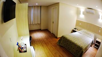 A compact hotel room with a bed, bedside table, and a small desk with a chair.