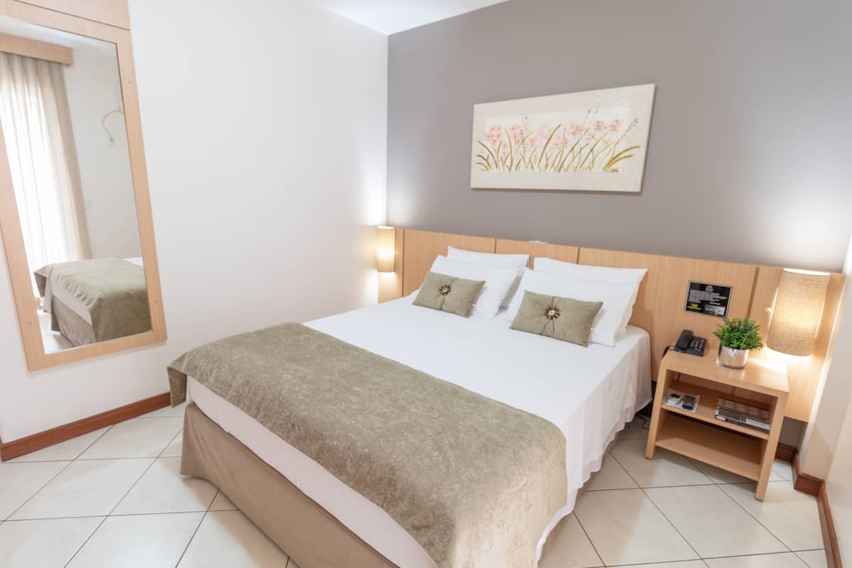 Une chambre d’hôtel bien aménagée, avec un grand lit, des lampes de chevet, une table de chevet ornée d’une plante et un miroir au mur.