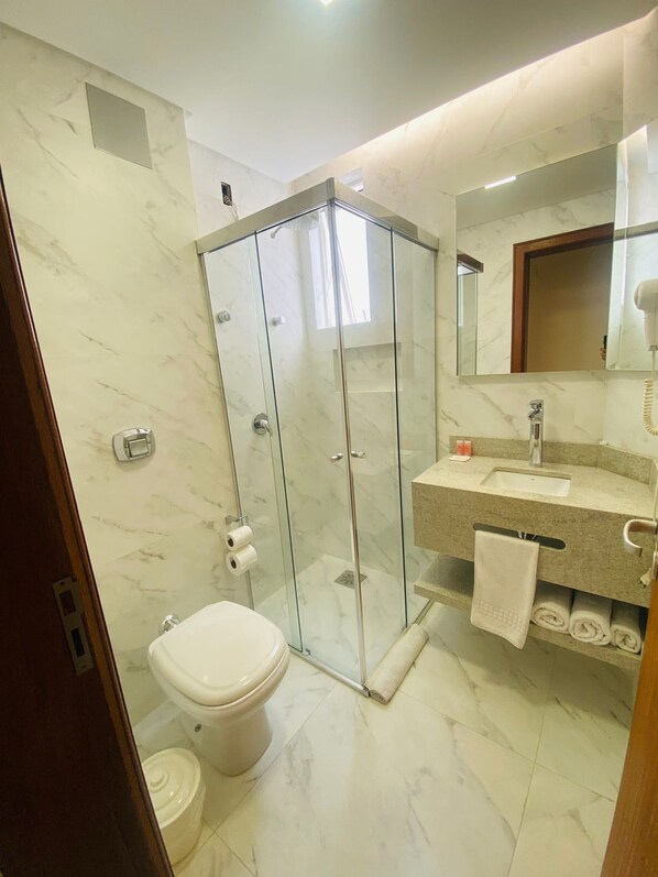 A modern bathroom with a glass-enclosed shower, a toilet, a sink with a mirror above, and a towel rack. - Diaudi Hotel (Sao Jose)