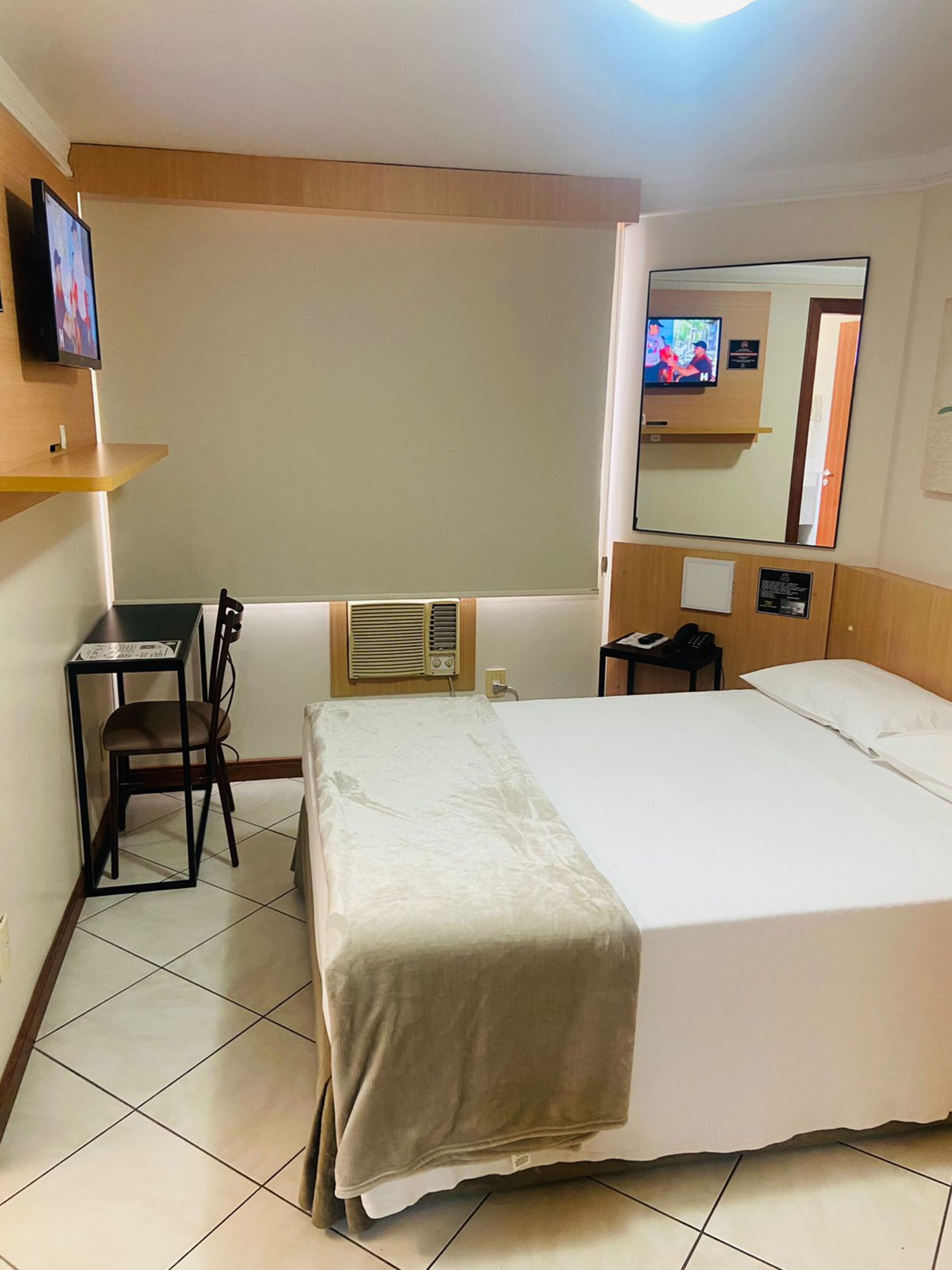 Hotellihuone, jossa on sänky, työpöytä tuolilla, televisio ja peili.