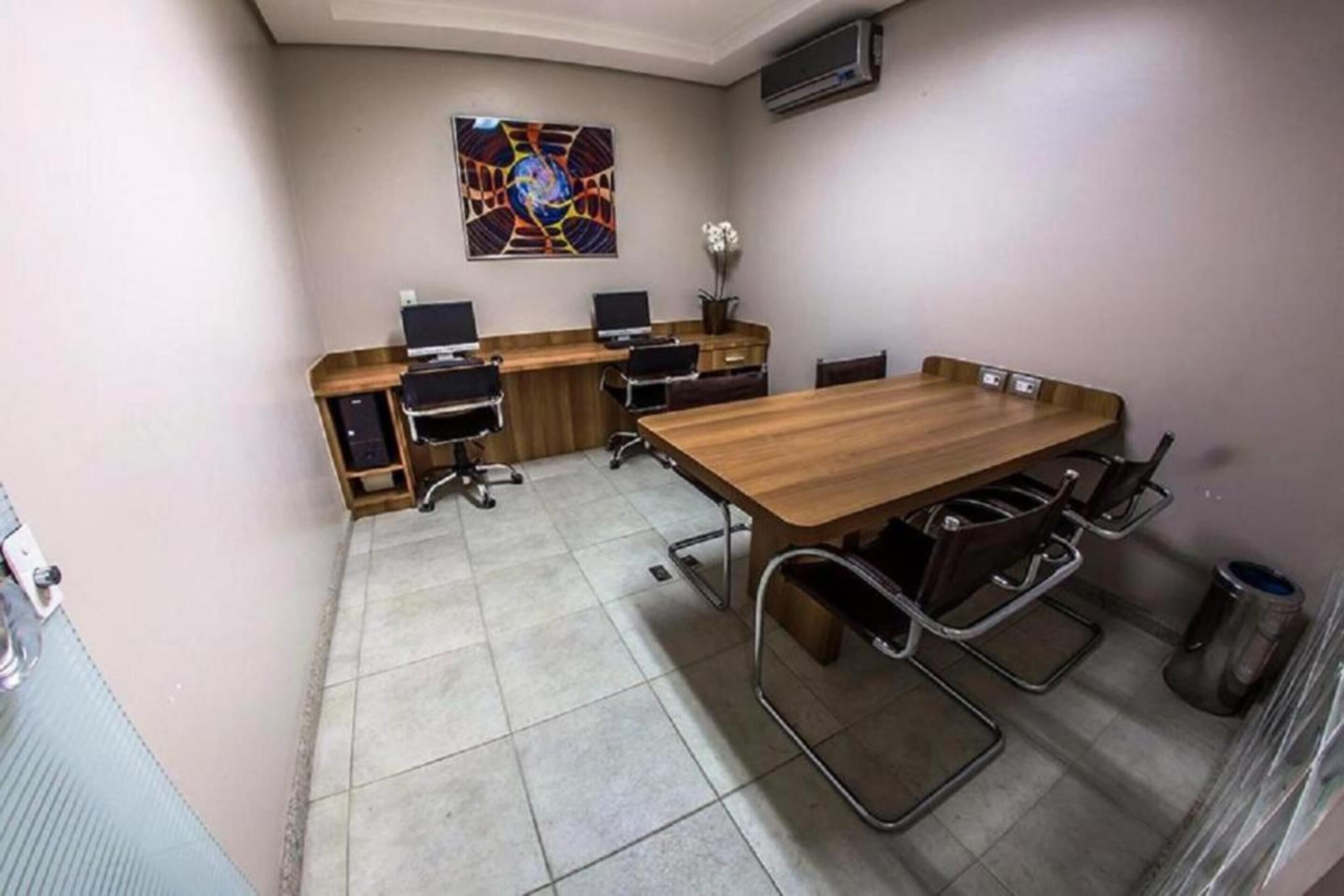Een vergaderzaal met een lange houten tafel, vier stoelen, twee laptops en een decoratieve vaas.