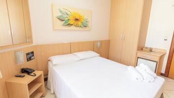 Hotellihuone, jossa on sänky, työpöytä puhelimineen, pieni kaappi ja seinällä auringonkukkaa esittävä taulu.