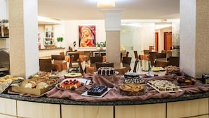 A buffet setup with various desserts and pastries, with a dining area in the background. - Diaudi Hotel (Sao Jose)