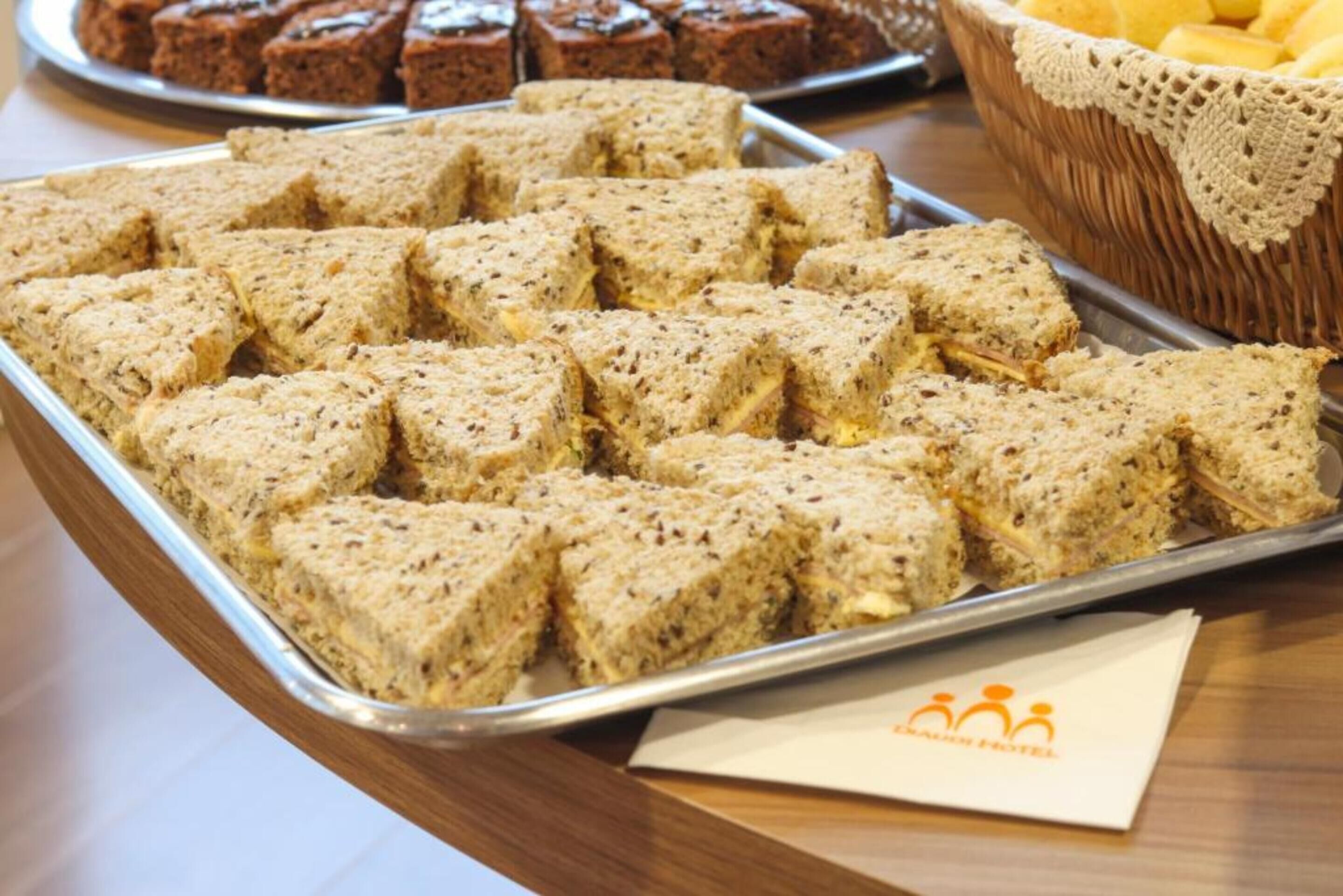 A tray of square-shaped, textured food items on a metal tray, with a wicker basket and a napkin with a logo in the background.