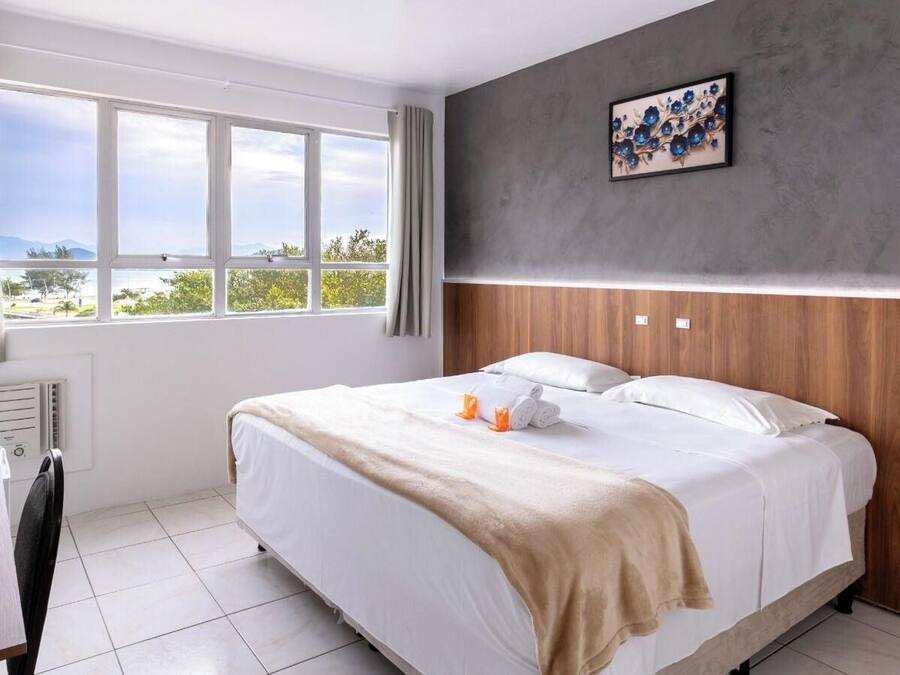Habitación de hotel con cama, escritorio, ventana con cortinas, radiador y un cuadro colgado en la pared.
