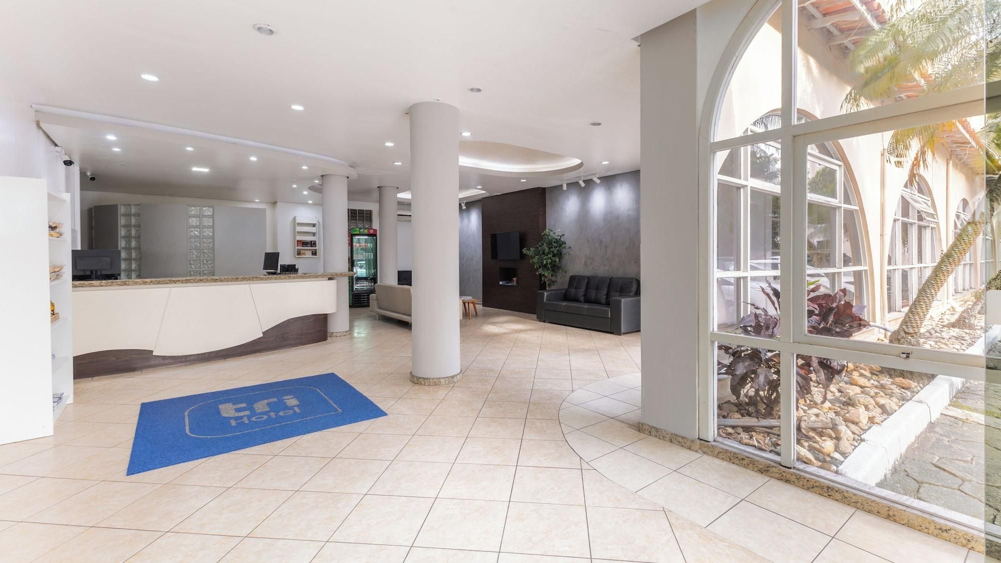 Um saguão de hotel com balcão de recepção, área de estar e grandes janelas.