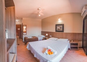 Une chambre d’hôtel avec un grand lit, deux tables de chevet, un ventilateur de plafond et un climatiseur fixé au mur.