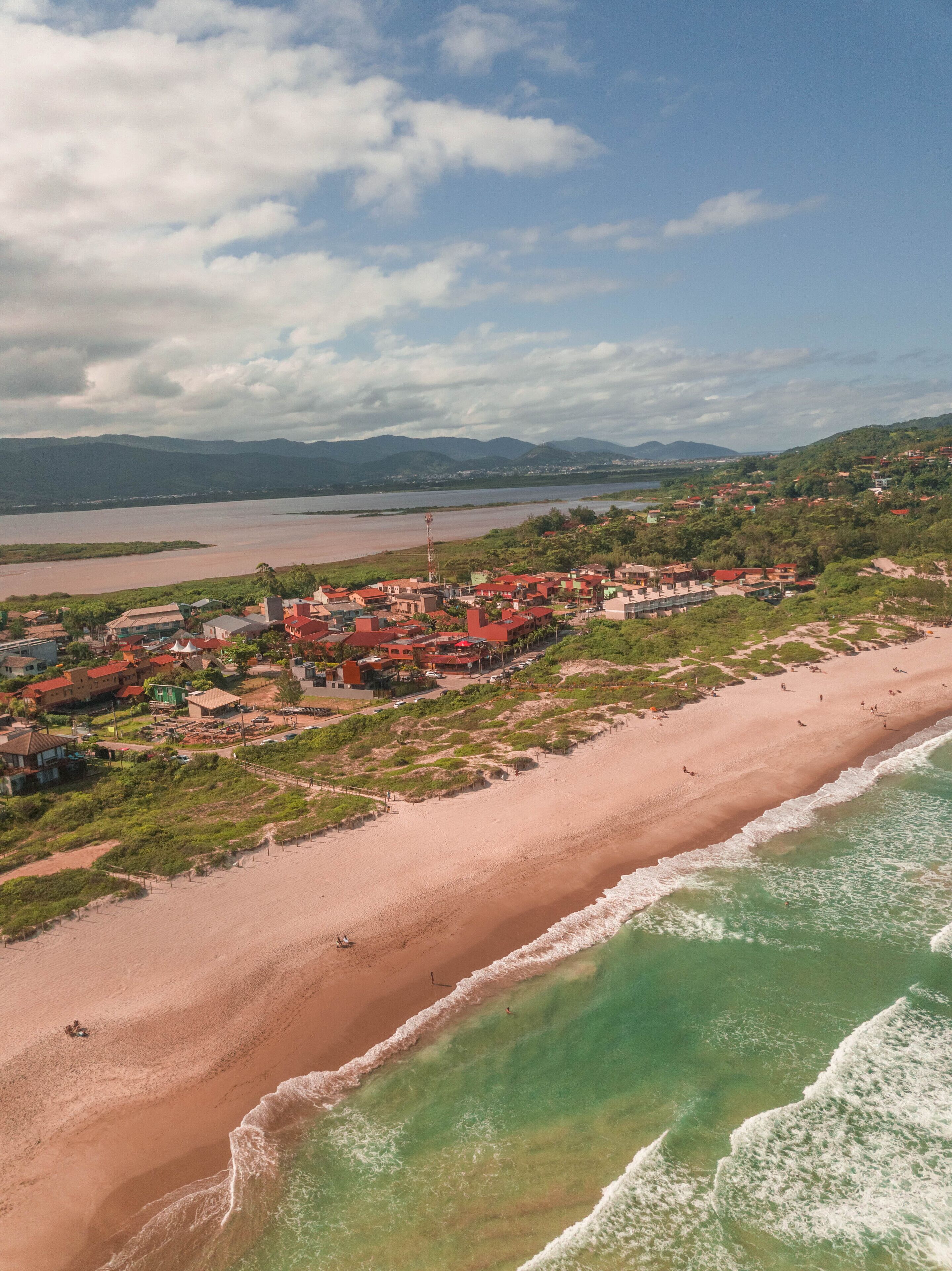 An aerial view of a coastal town with a beach, houses, and a river.