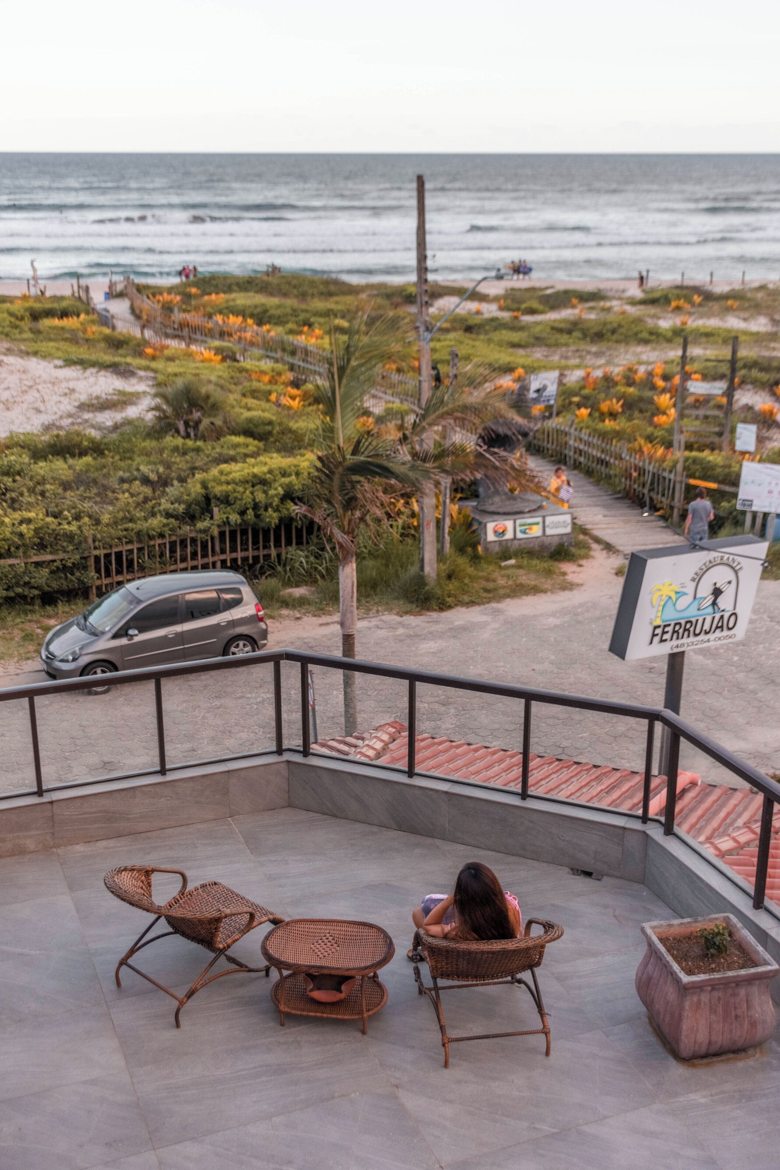 A balcony with wicker furniture overlooking a beach and ocean.
