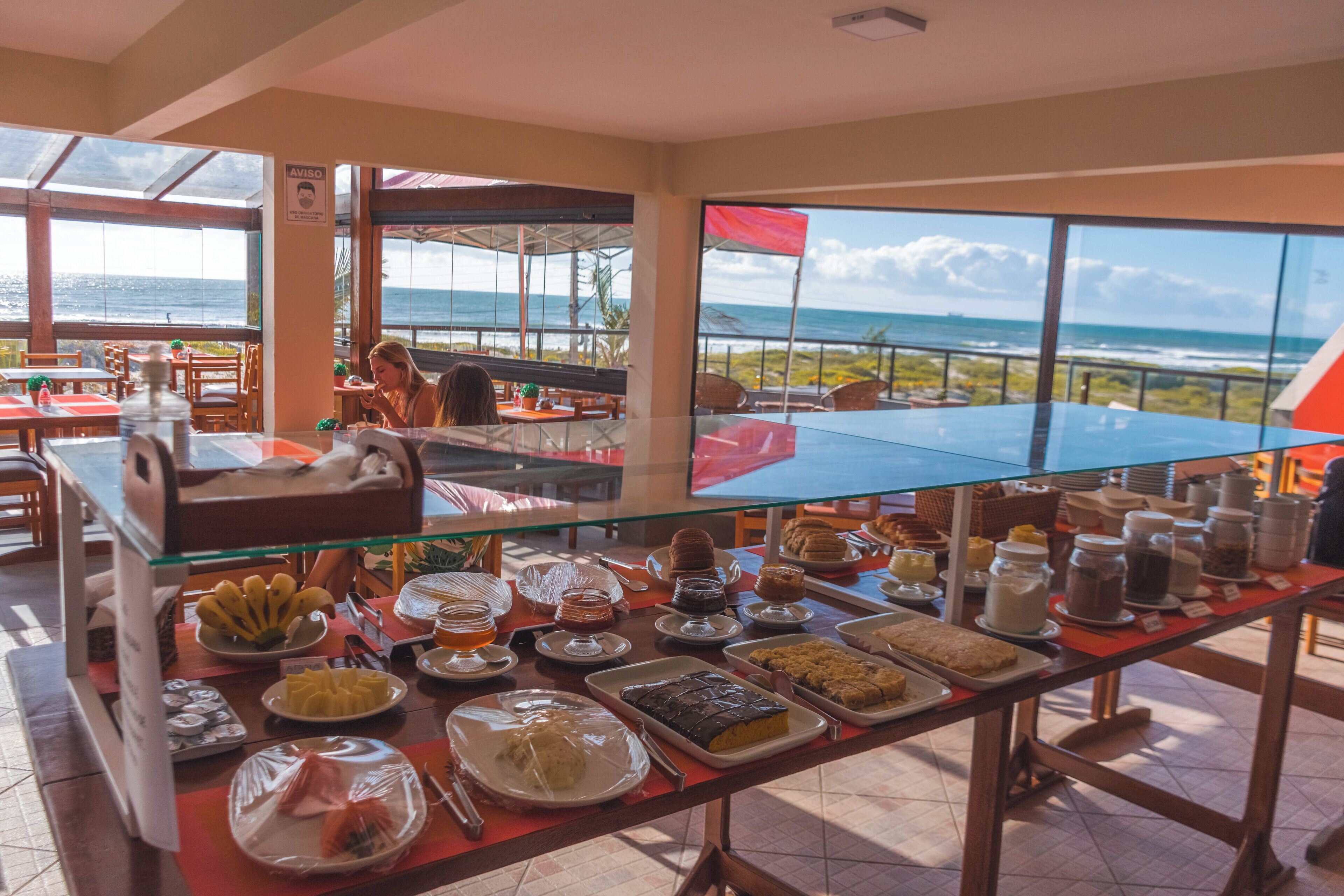 Une table de buffet proposant une variété de plats, avec une vue sur l’océan grâce à de grandes fenêtres.