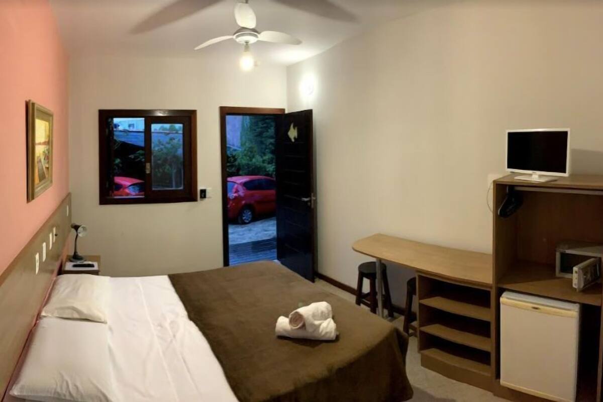 Une chambre d’hôtel avec un lit, un bureau, une télévision et une vue sur une voiture rouge, visible par la fenêtre.