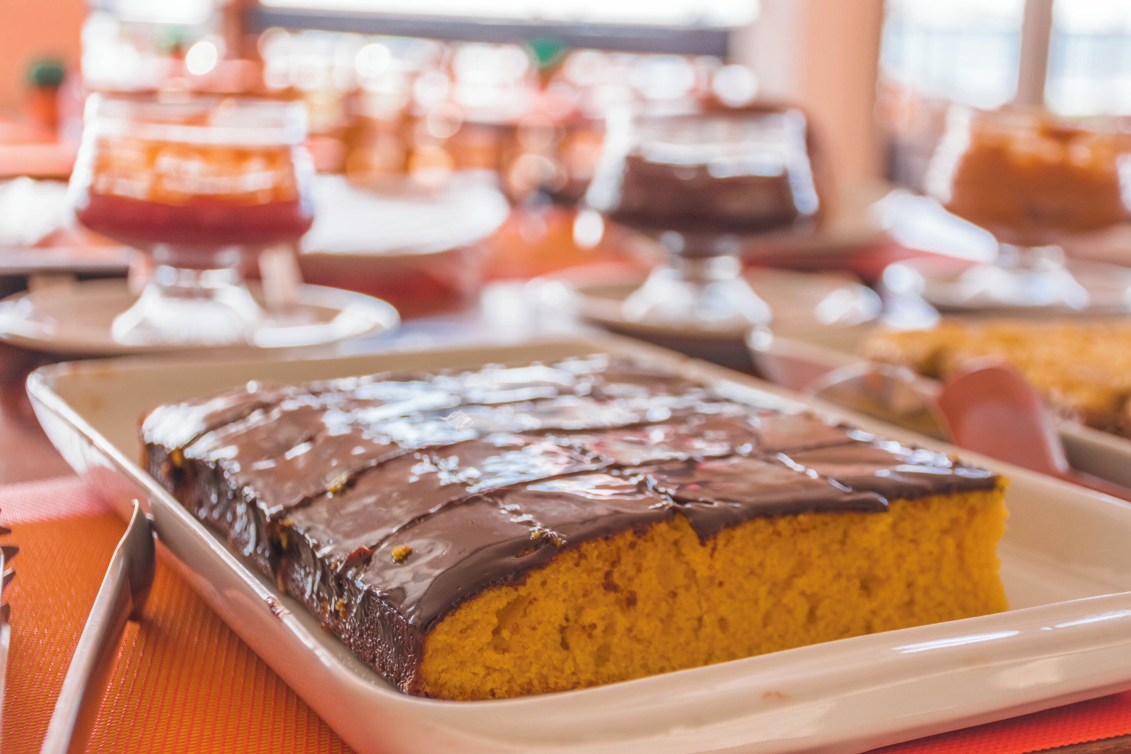 Un vassoio con dolci, tra cui una torta ricoperta di cioccolato su un piatto bianco, su una tovaglia arancione.