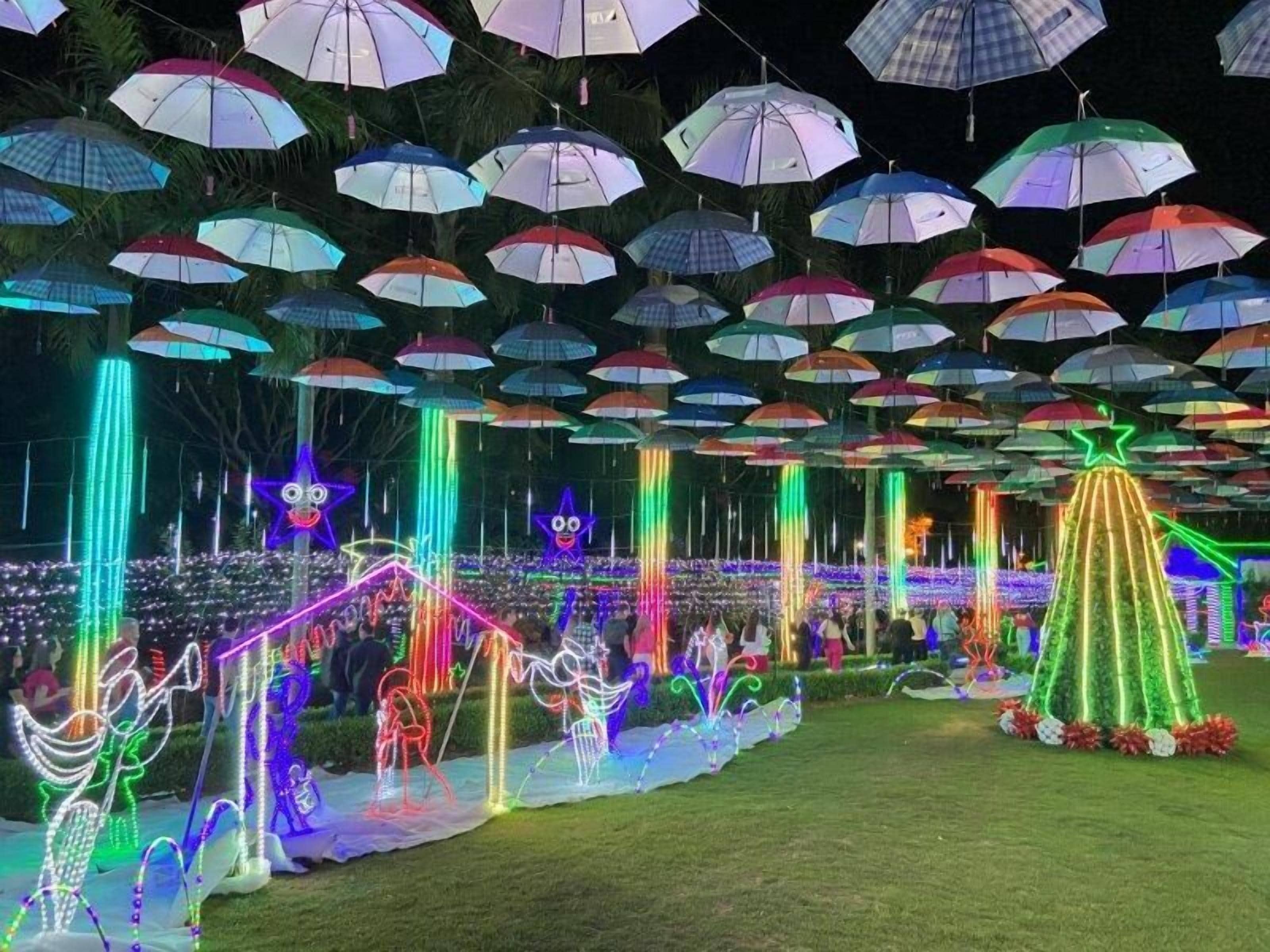 Escena festiva al aire libre con muchos paraguas y decoraciones iluminadas.