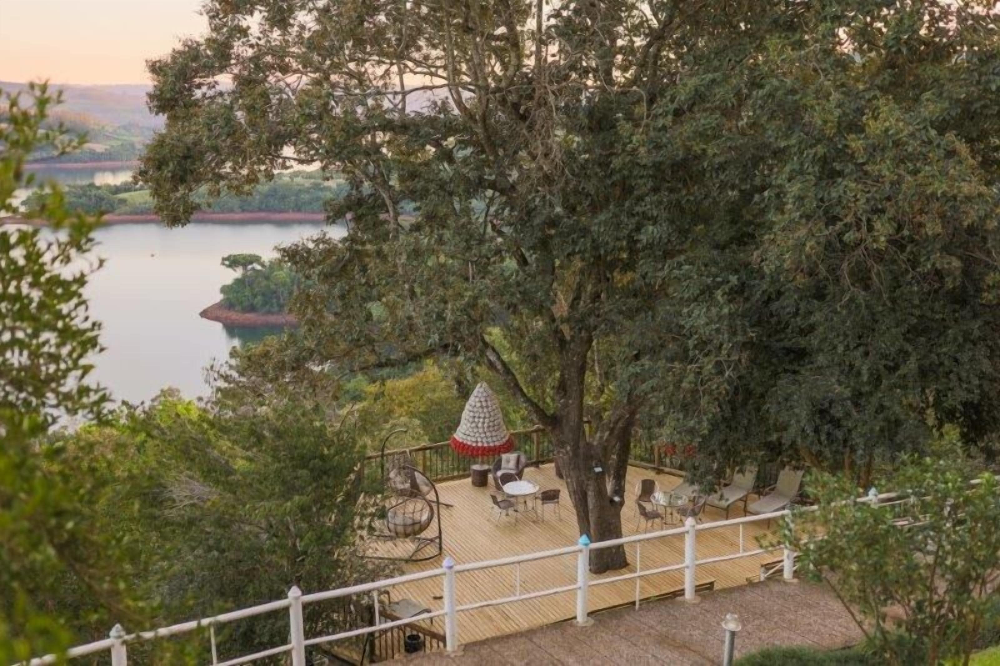A deck with outdoor seating and a conical structure, overlooking a body of water and surrounded by trees.