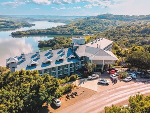 Un hotel con terraza en la azotea, zona de aparcamiento y vistas a un lago y colinas.