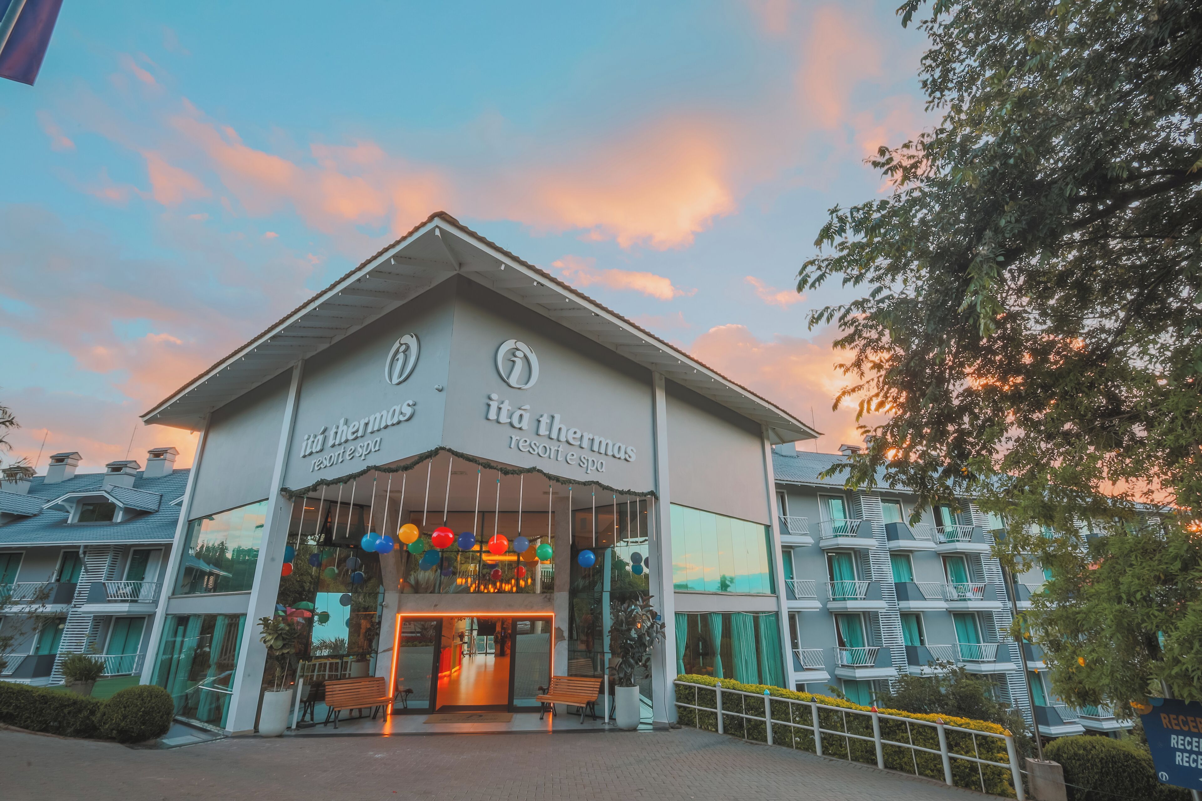 A hotel entrance with a sign reading 'itá thermas resort spa,' a balcony with seating, and a clear sky.