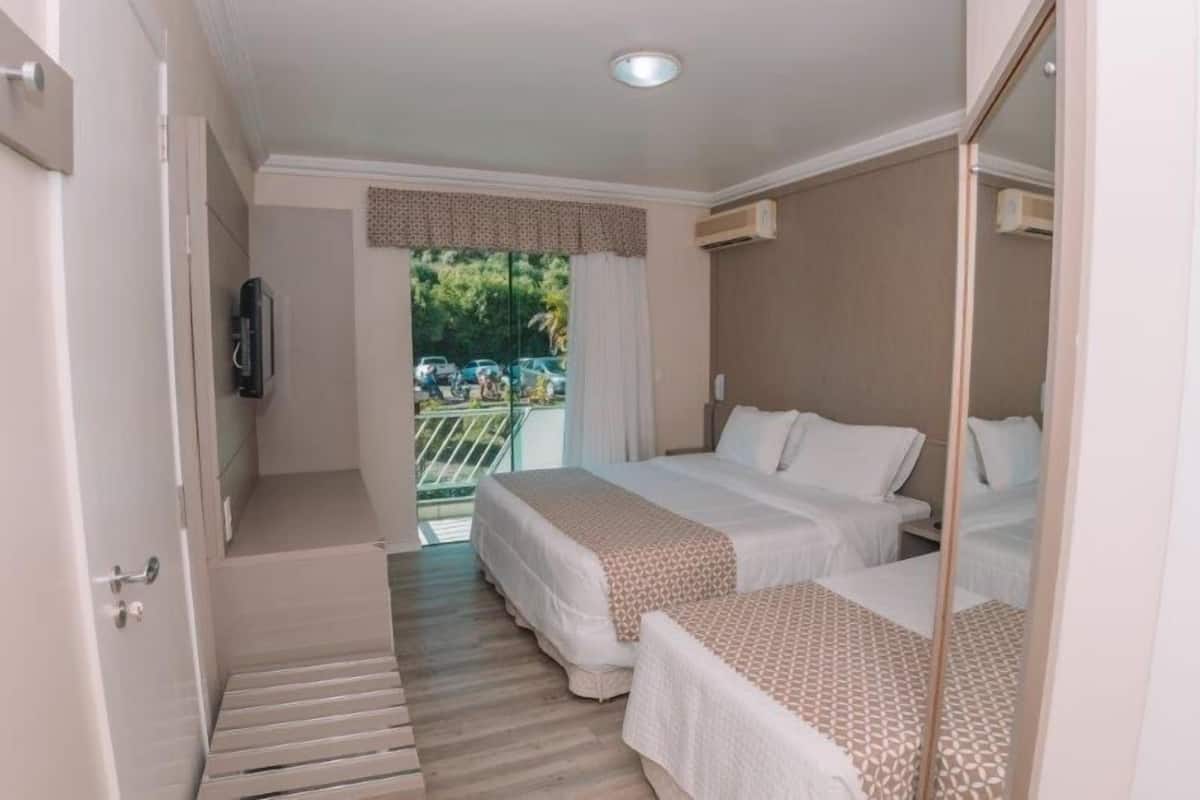 A hotel room with two beds, a balcony with a view, and a television on the wall.