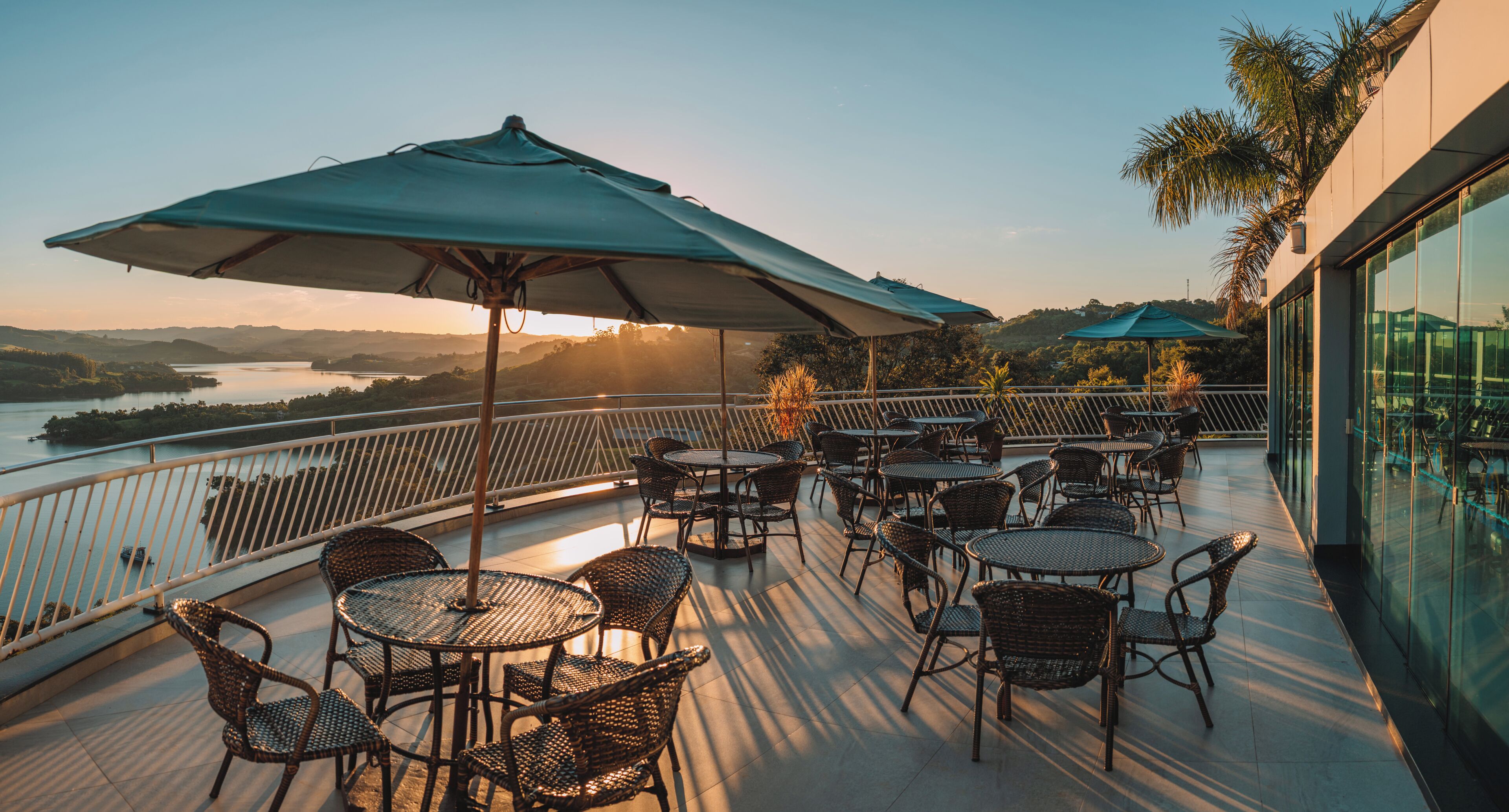 A terrace with tables and chairs, overlooking a body of water and hills.