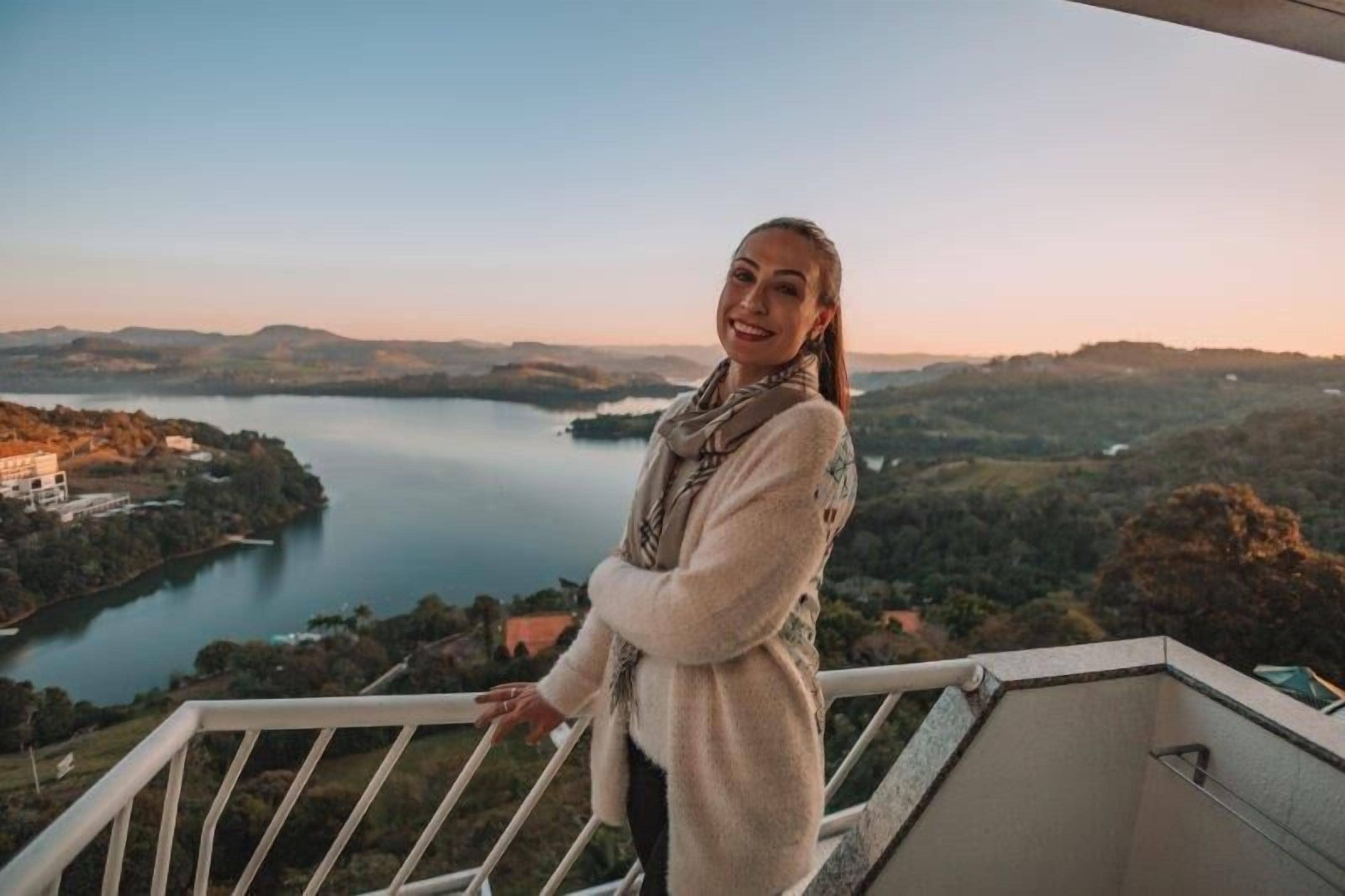 A person standing on a balcony overlooking a lake and hills.