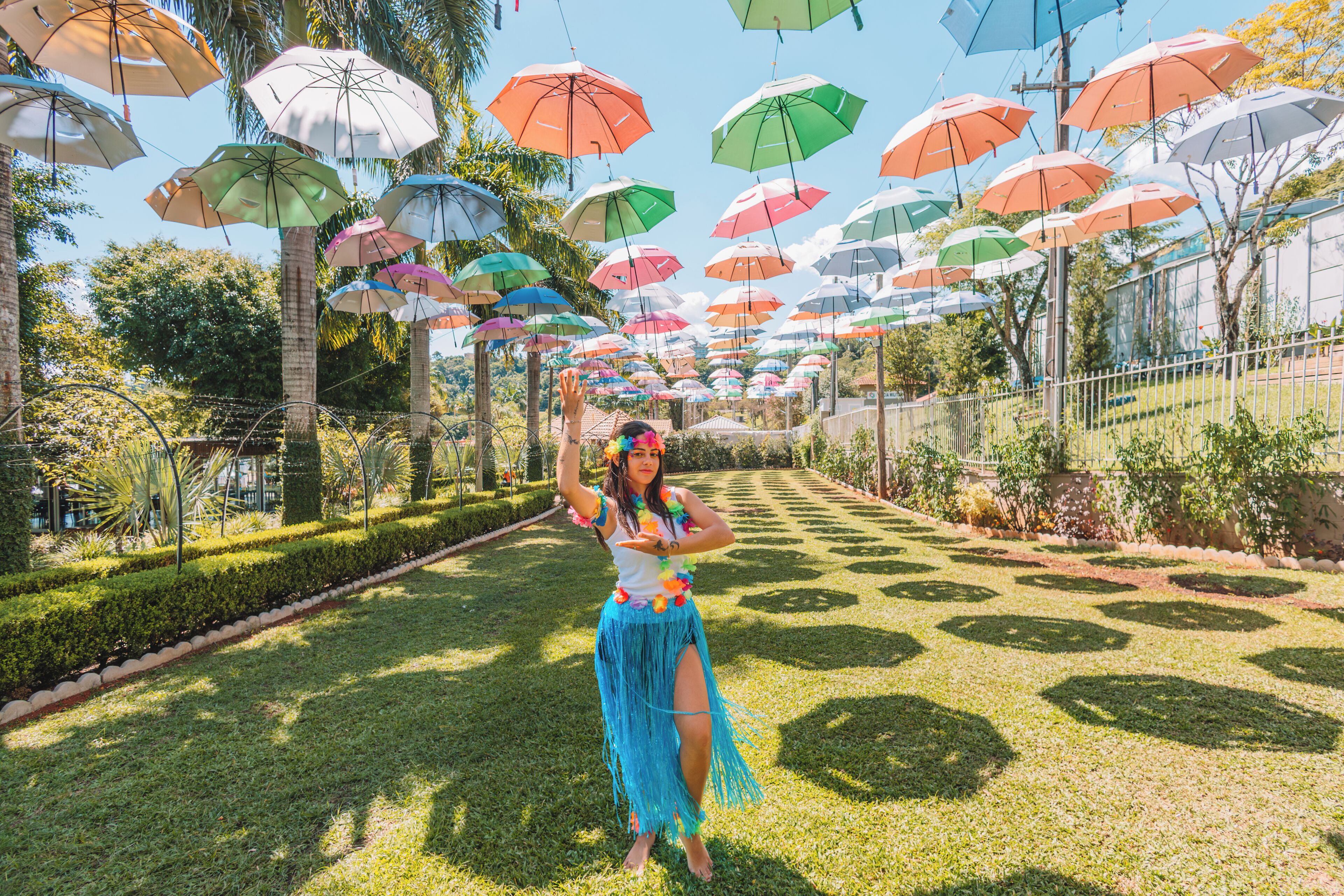 A pathway lined with trees and a person in a blue skirt and floral headpiece.