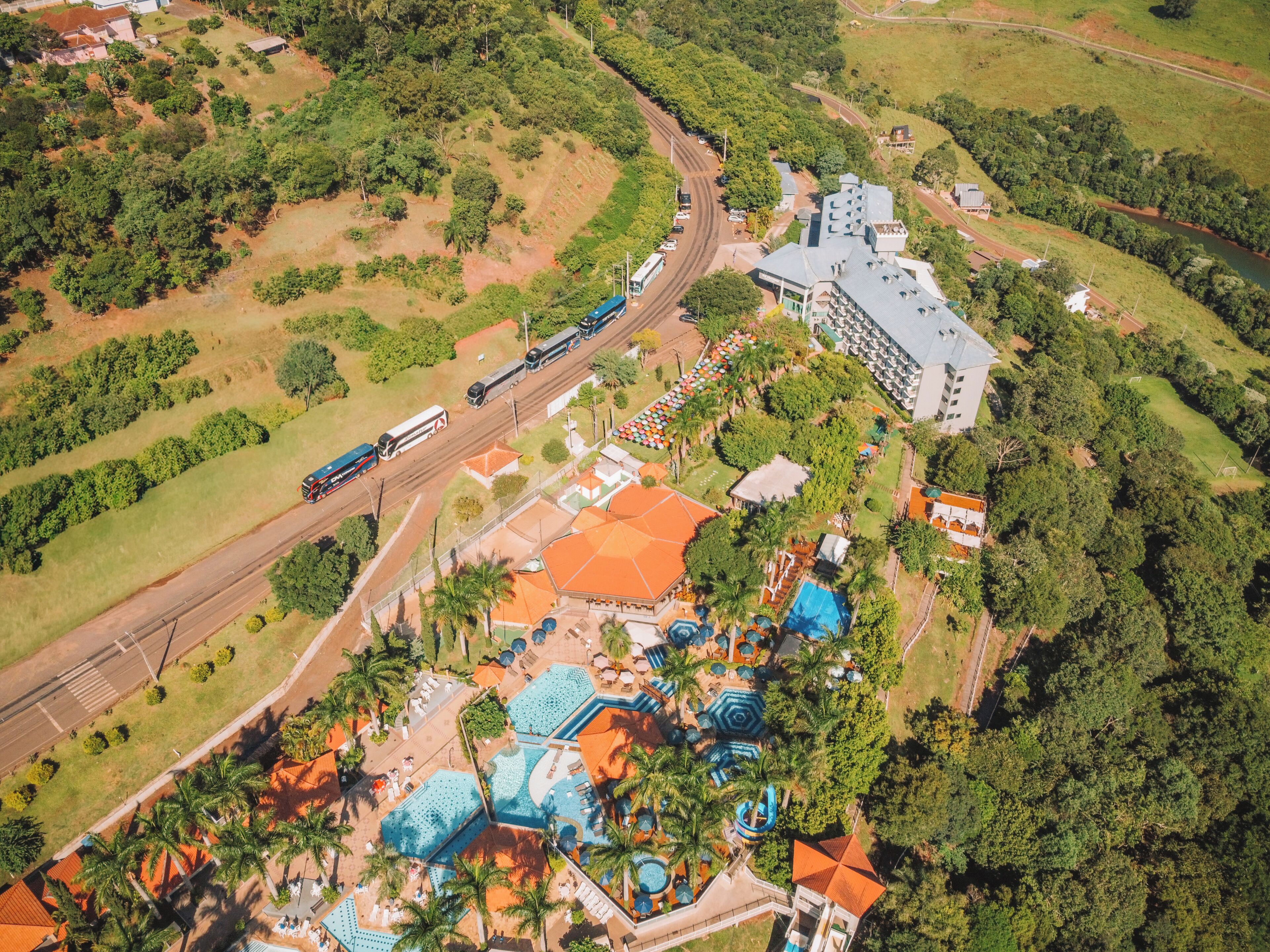 Eine Luftaufnahme eines Resorts mit Poolbereich, Bushaltestelle und einem großen Gebäude mit geneigtem Dach.
