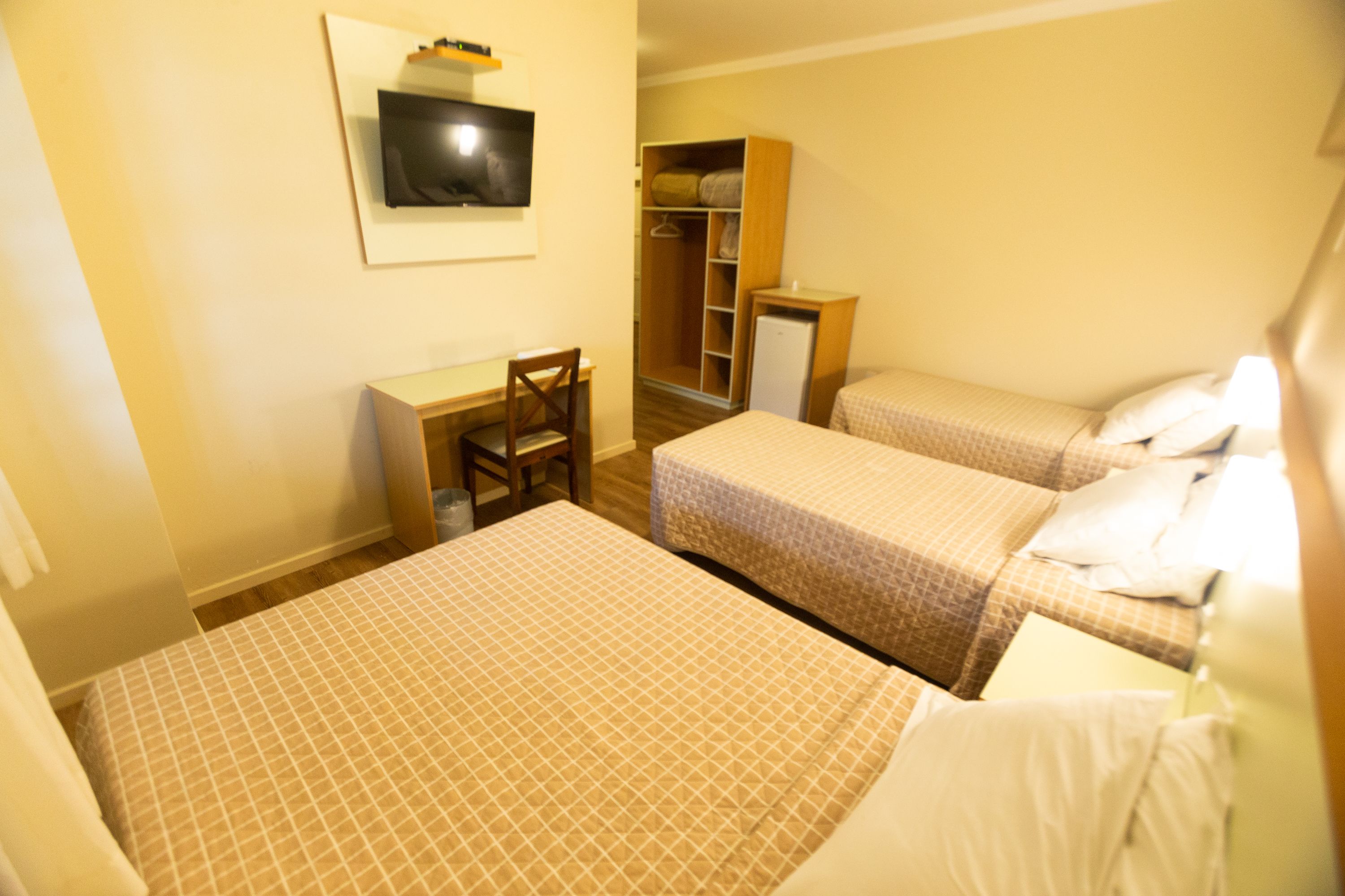 Una habitación de hotel con dos camas, un escritorio, una silla, un armario y un televisor.