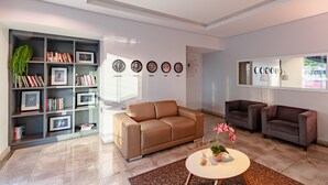 A modern living room with a brown leather sofa, a bookshelf, a coffee table with flowers, and two armchairs.