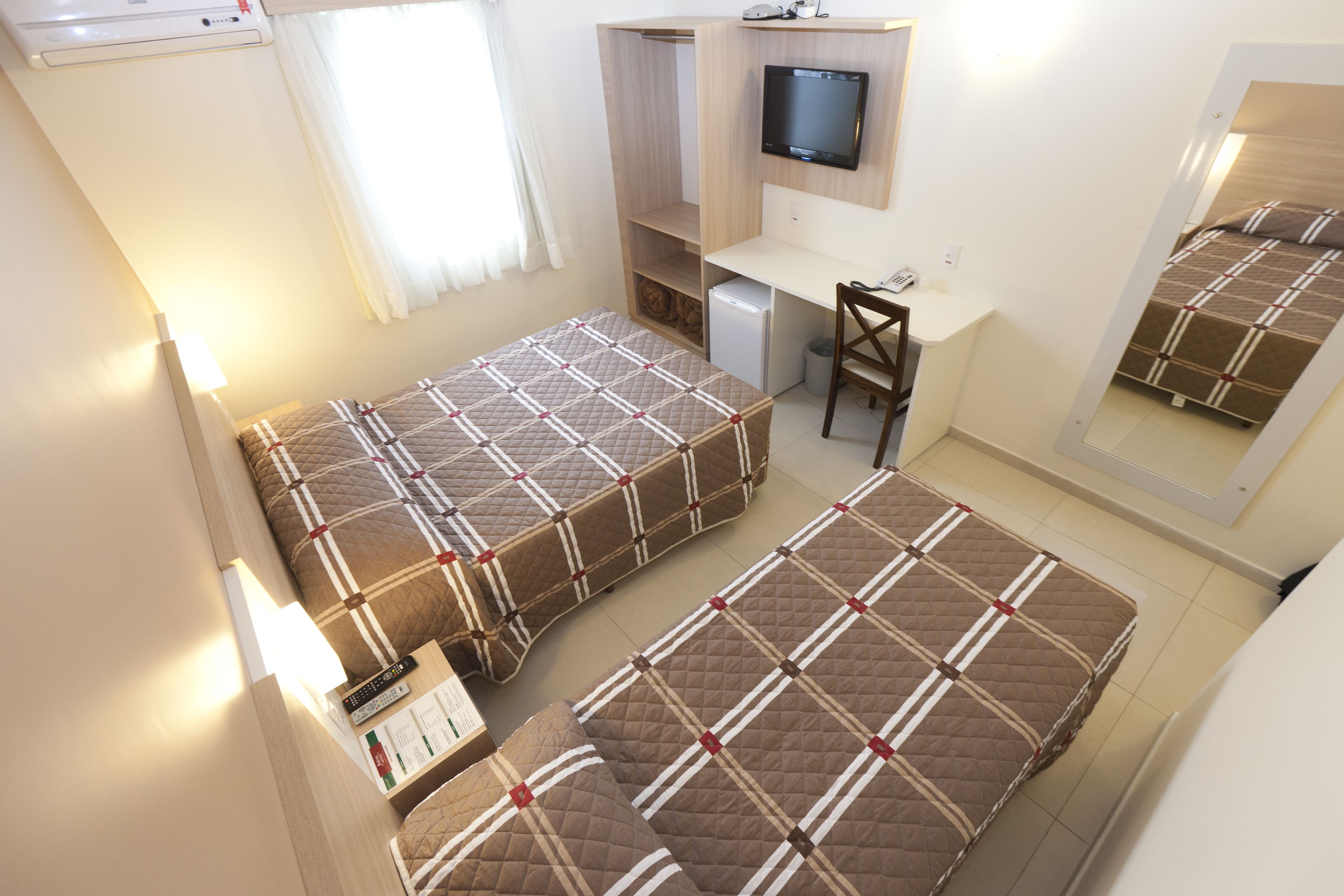 A compact room with two beds, a desk, a television, and a small refrigerator.