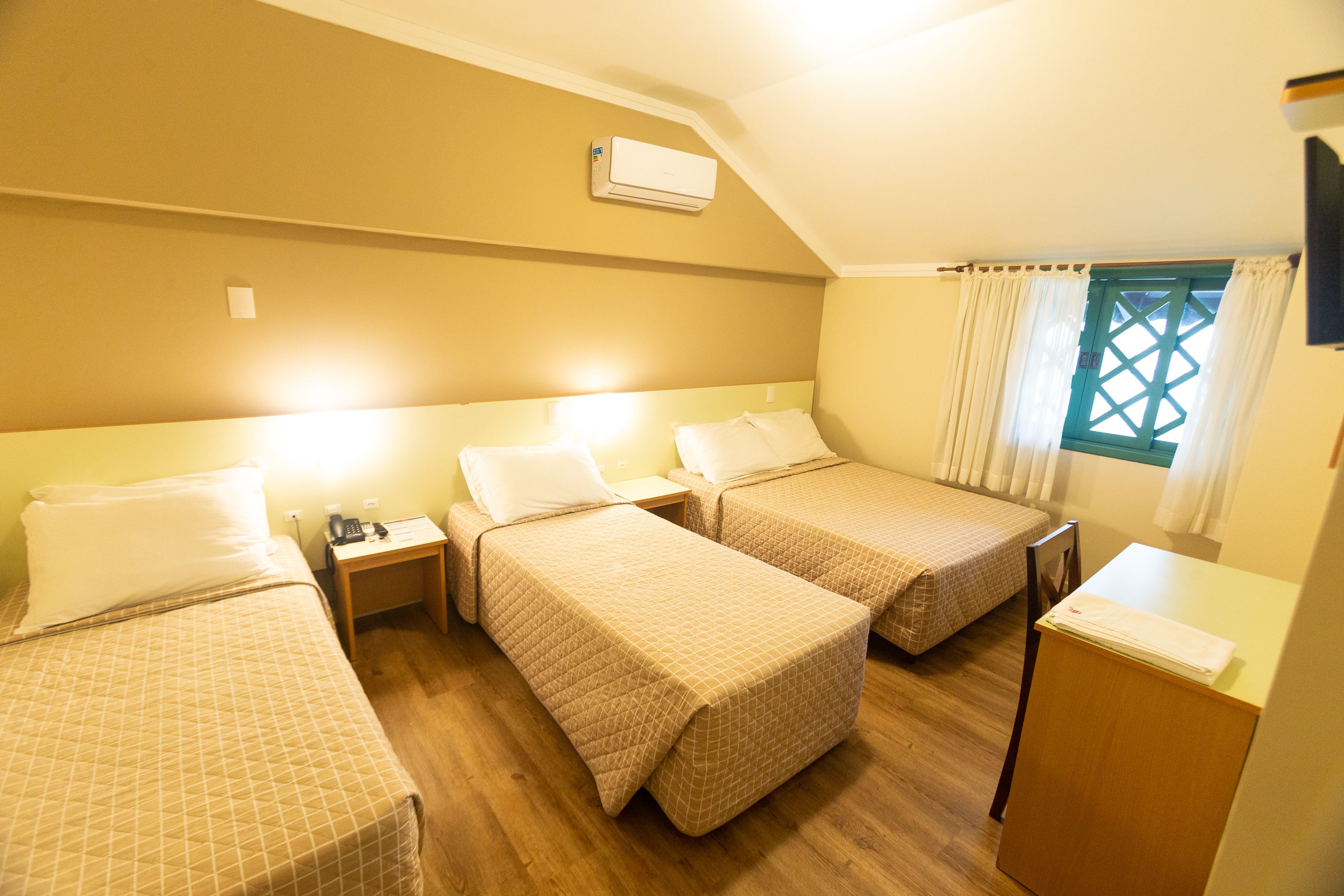 Habitación de hotel con dos camas individuales, un escritorio pequeño, una silla y una ventana con cortinas.