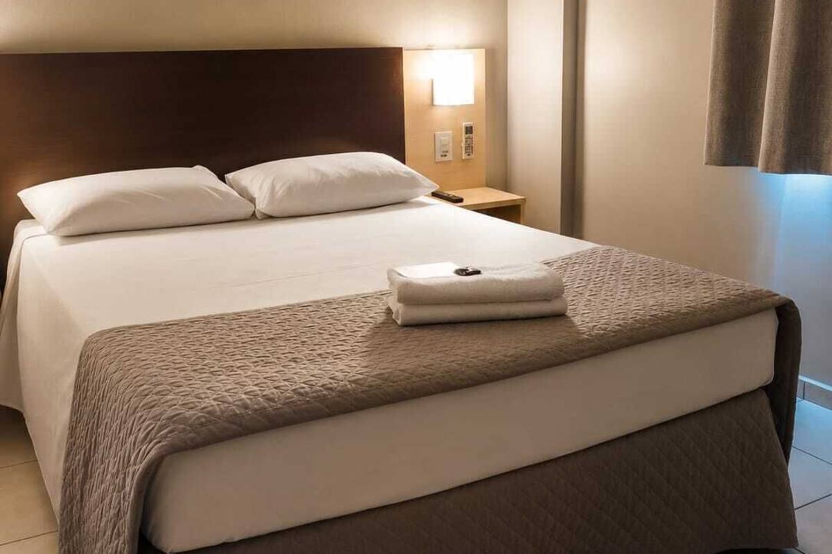 Ein Hotelzimmer mit einem großen Bett, einem Nachttisch mit Lampe und einem Vorhang am Fenster.