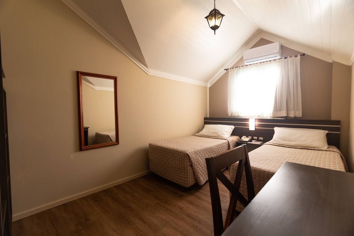 Ein Schlafzimmer mit zwei Einzelbetten, einem Holztisch, einem Stuhl, einem Spiegel und einer Deckenleuchte.