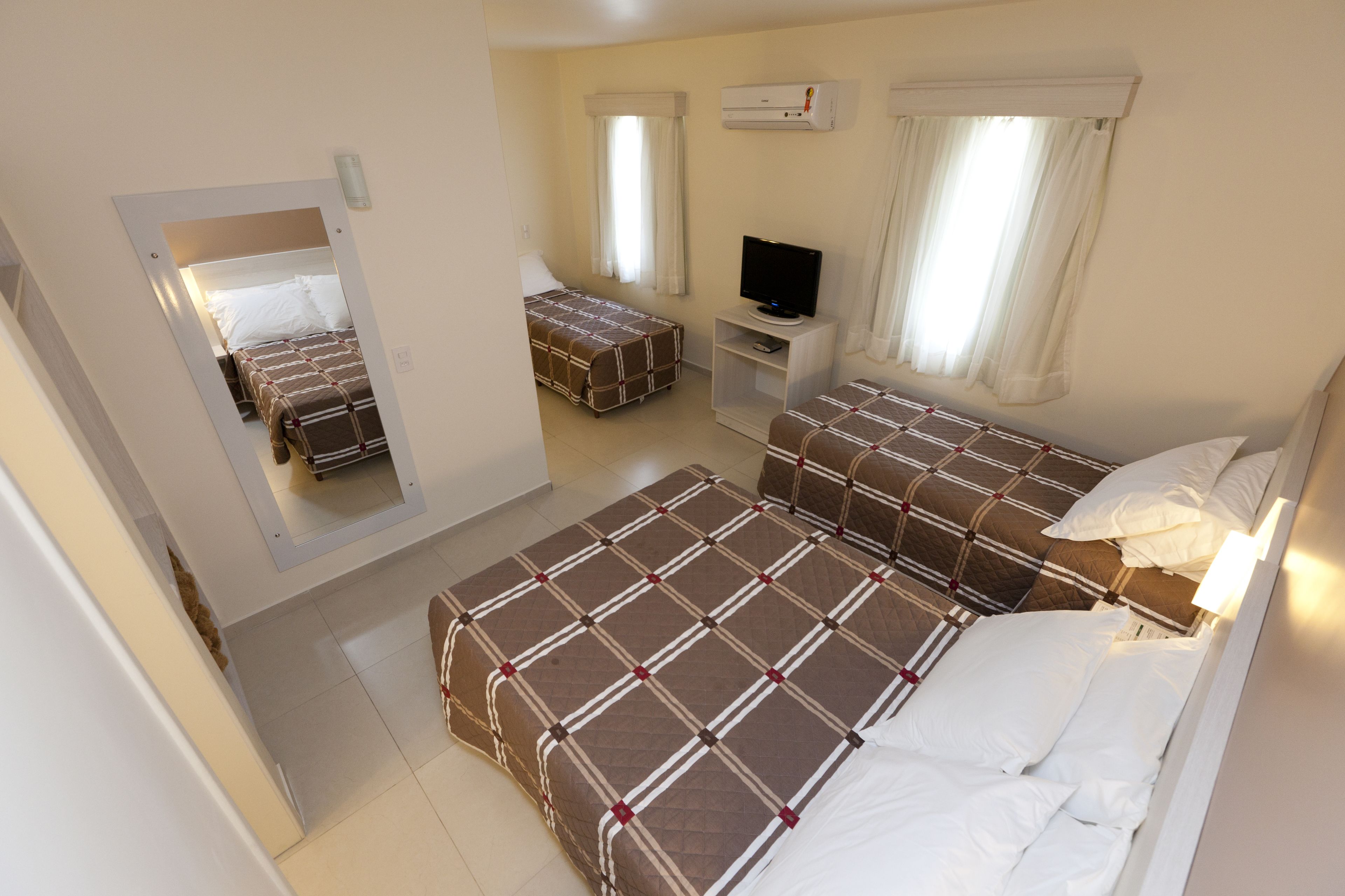 A hotel room with two beds, a TV, and a mirror.
