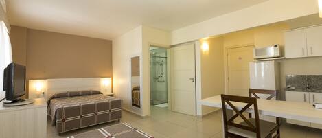Una habitación de hotel compacta con cama, escritorio, silla, televisión y kitchenette.
