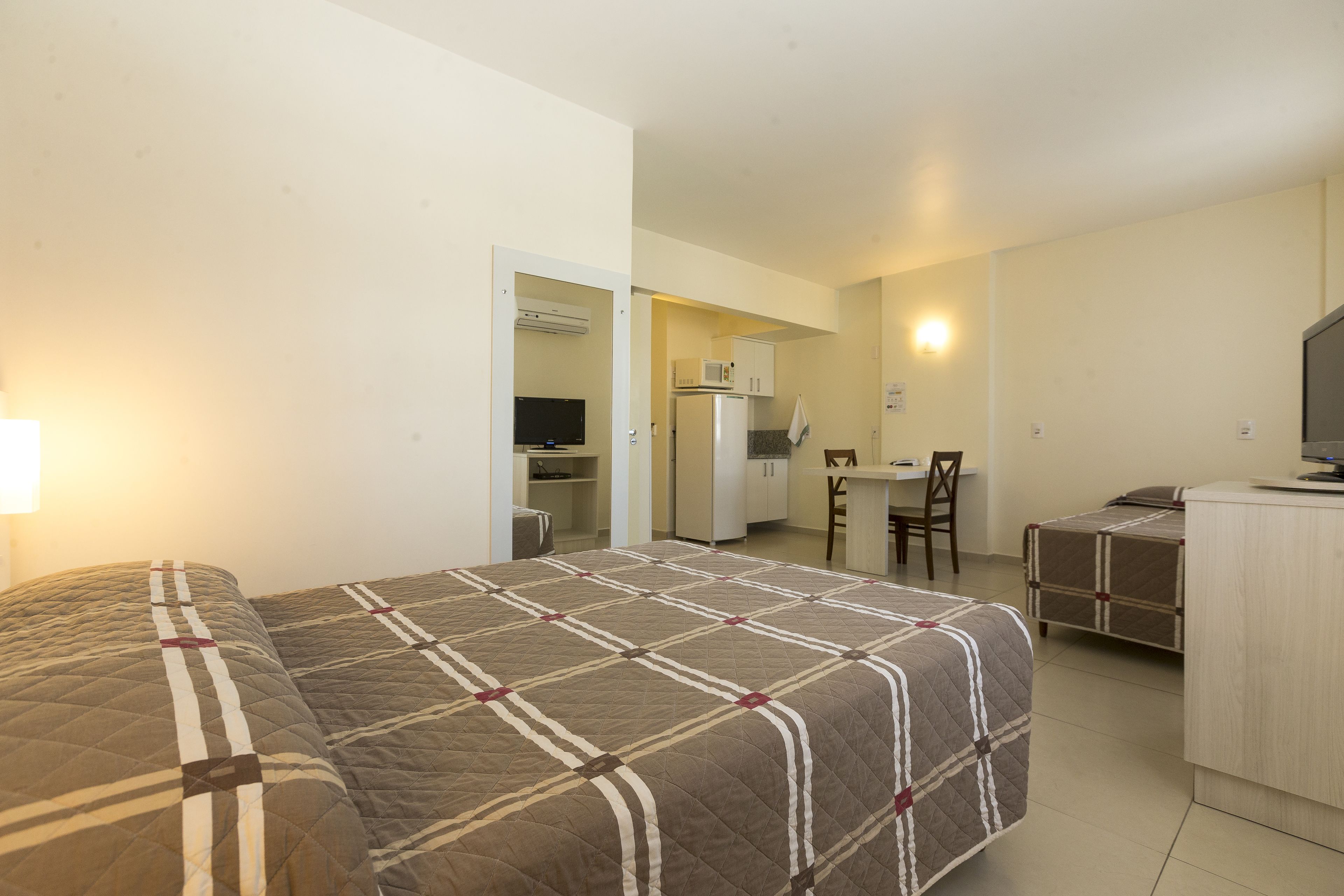 A hotel room with a bed, a desk, a chair, a refrigerator, and a microwave.