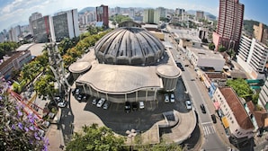 A large, dome-shaped building surrounded by modern high-rise buildings, with a parking area in front.