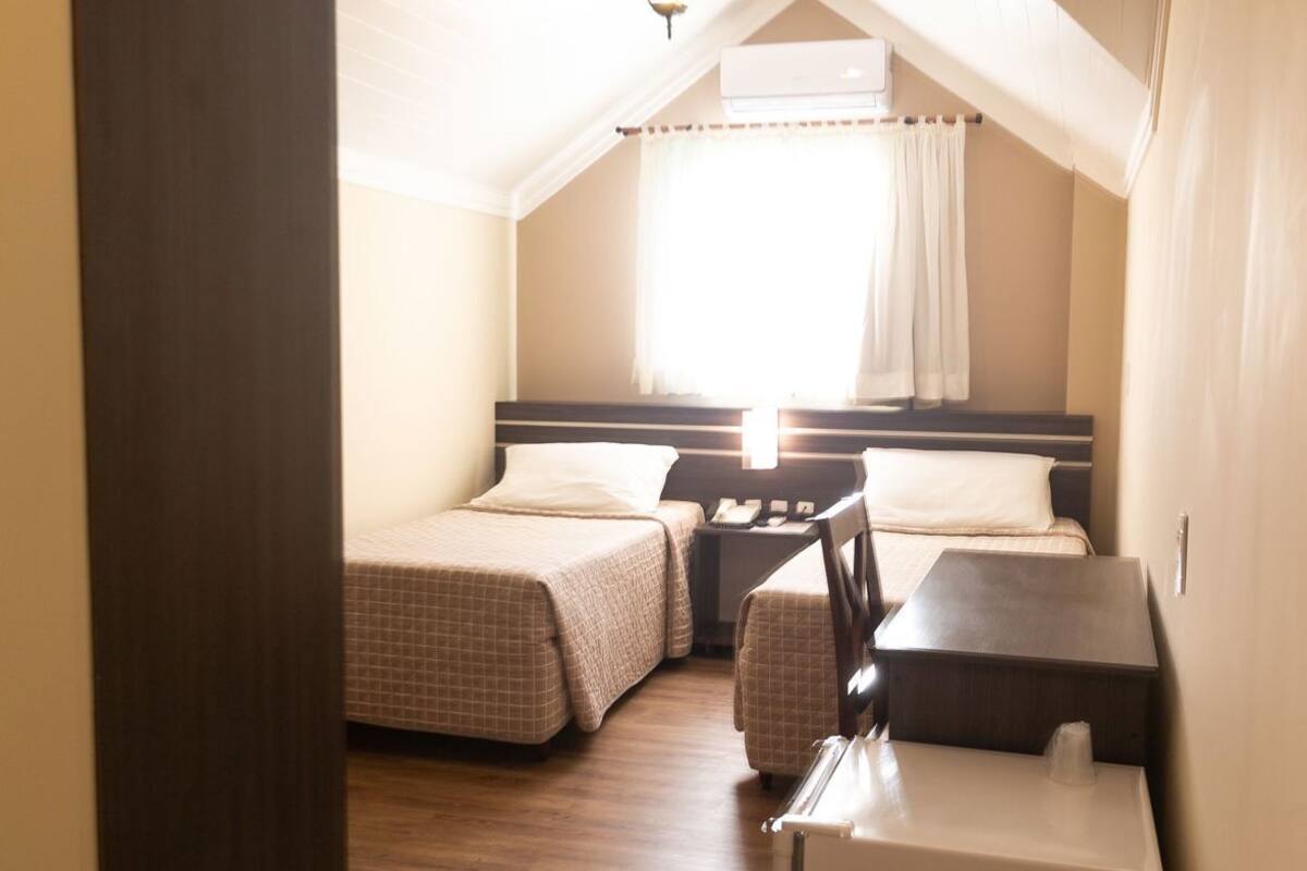 Een knus zolderkamertje met twee bedden, een bureau en een koelkast.
