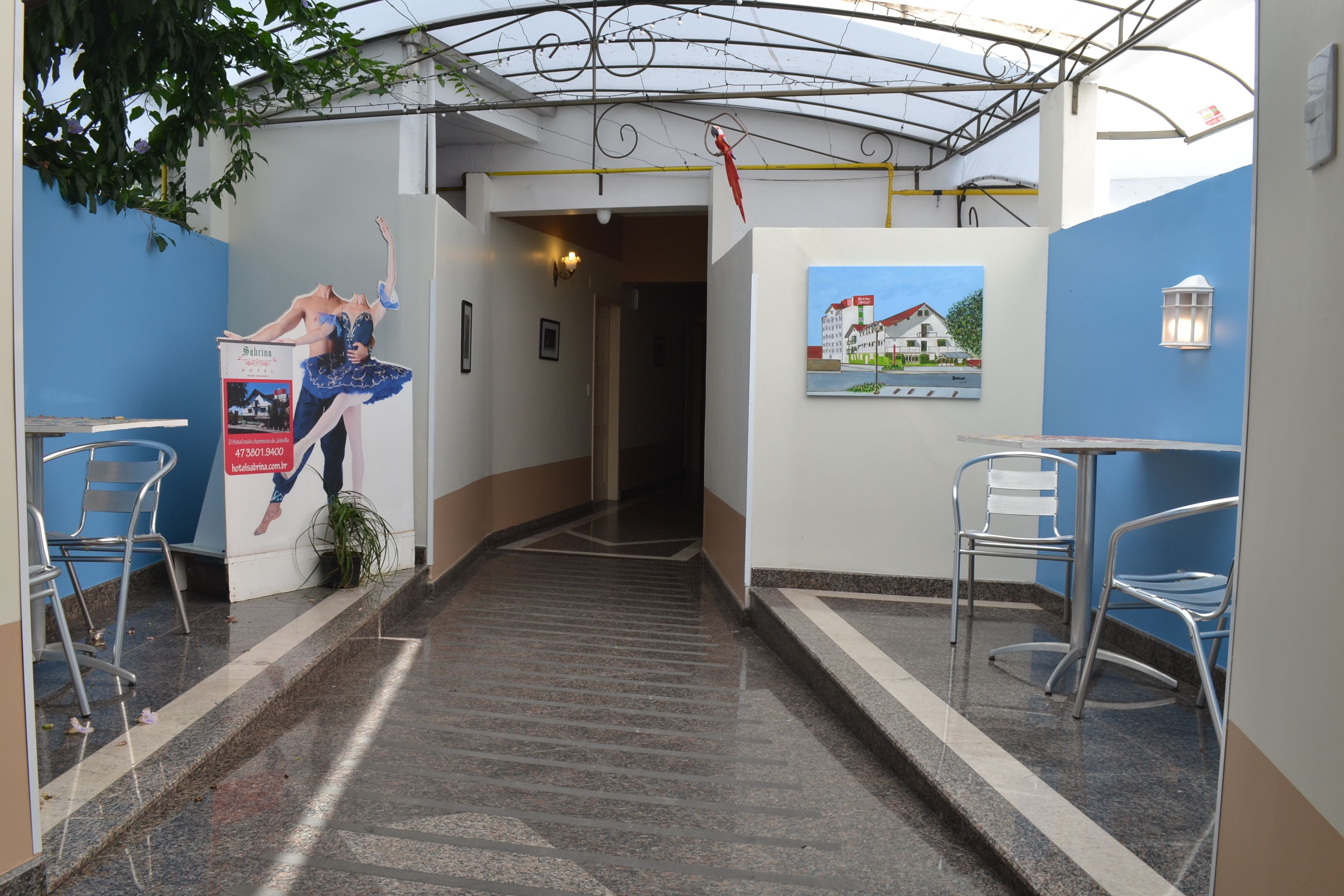 A hotel corridor with a staircase, metal chairs, a poster, and a painting on the wall.
