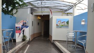 A hotel corridor with a staircase, metal chairs, a poster, and a painting on the wall.