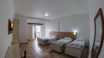 Une chambre d’hôtel avec trois lits, un bureau et une chaise. Il y a une fenêtre avec des rideaux, une porte et un miroir au mur.