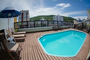 A rooftop swimming pool with lounge chairs and umbrellas, surrounded by a wooden deck and a cityscape view. - Flipper Hotel (Laguna)