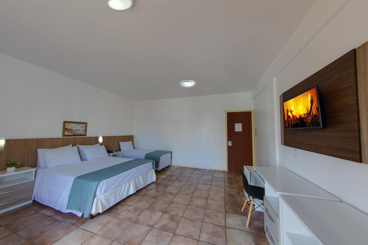 Quarto de hotel com duas camas, uma escrivaninha, uma televisão e uma porta.